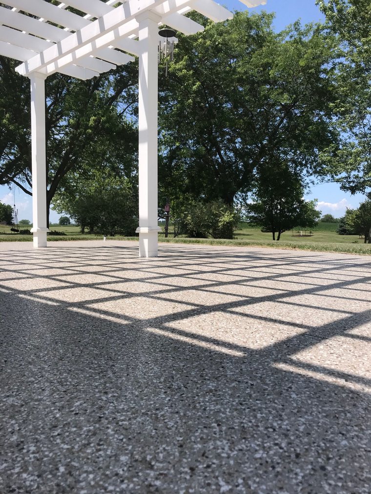 Coated patio under a white pergola, with shadow lines across the flake finish.