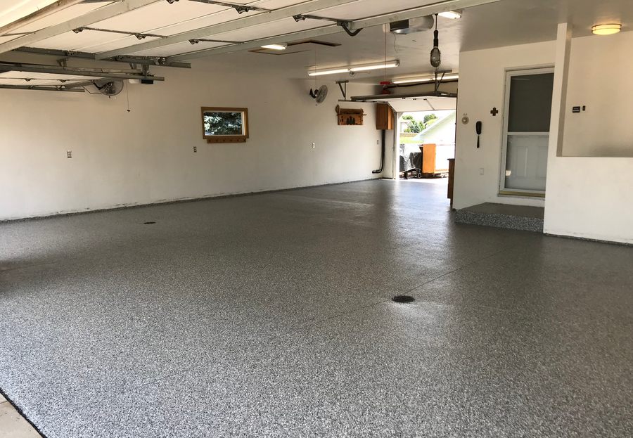Garage bay with the overhead door open and a flake floor running to the daylight.